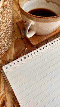 A ceramic coffee cup and spiral notebook on a textured wooden table. Cozy workspace feel.