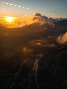 Breathtaking aerial view of sunset over mountains, clouds, and winding road.