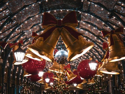 Free Golden bells and red ornaments under twinkling lights create a festive atmosphere in an arcade at night. Stock Photo
