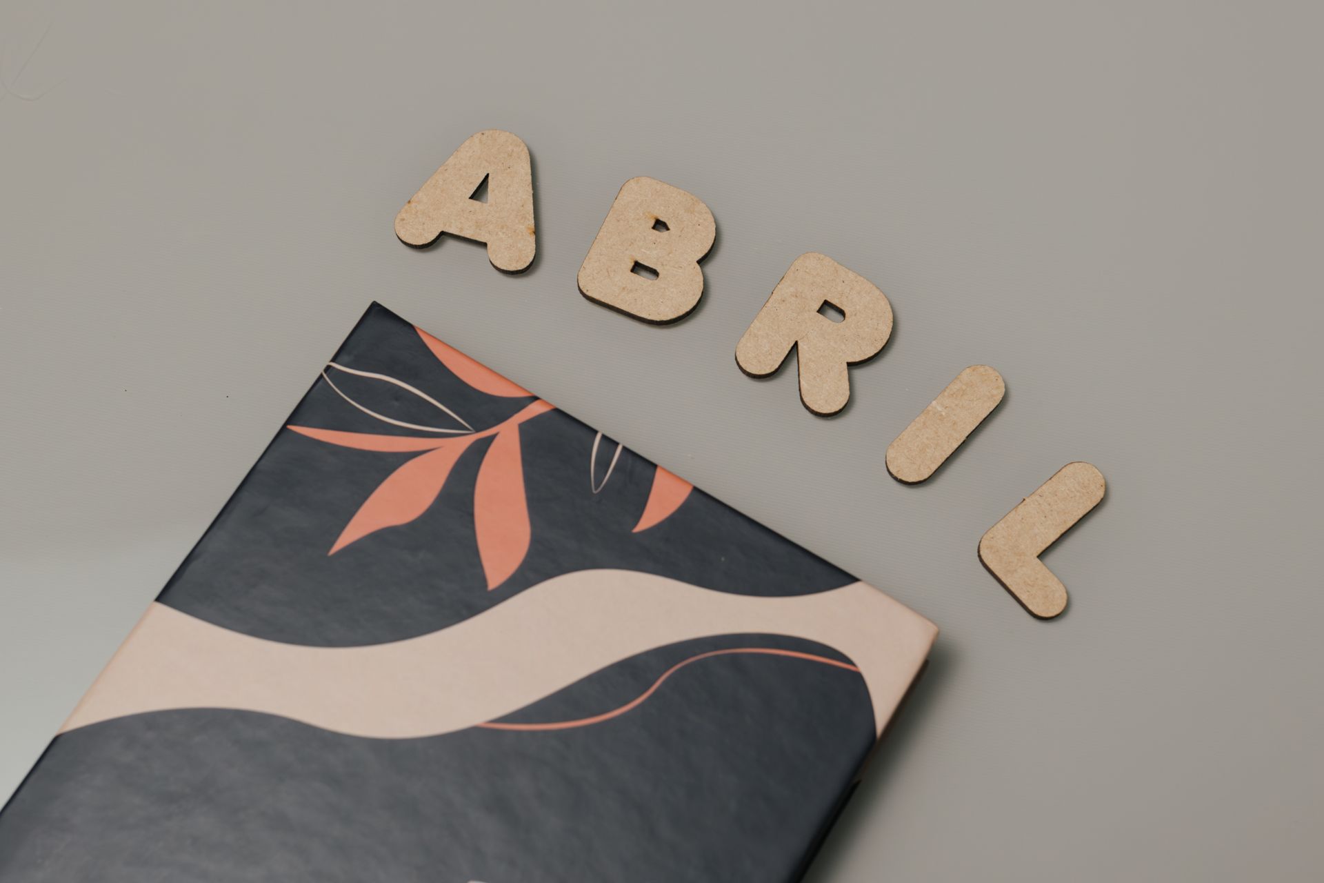 Wooden letters spelling Abril on a flat surface with abstract art cover beneath, creating a modern aesthetic.