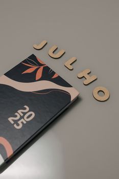 Abstract calendar and wooden letters spelling 'JULHO' on grey surface.