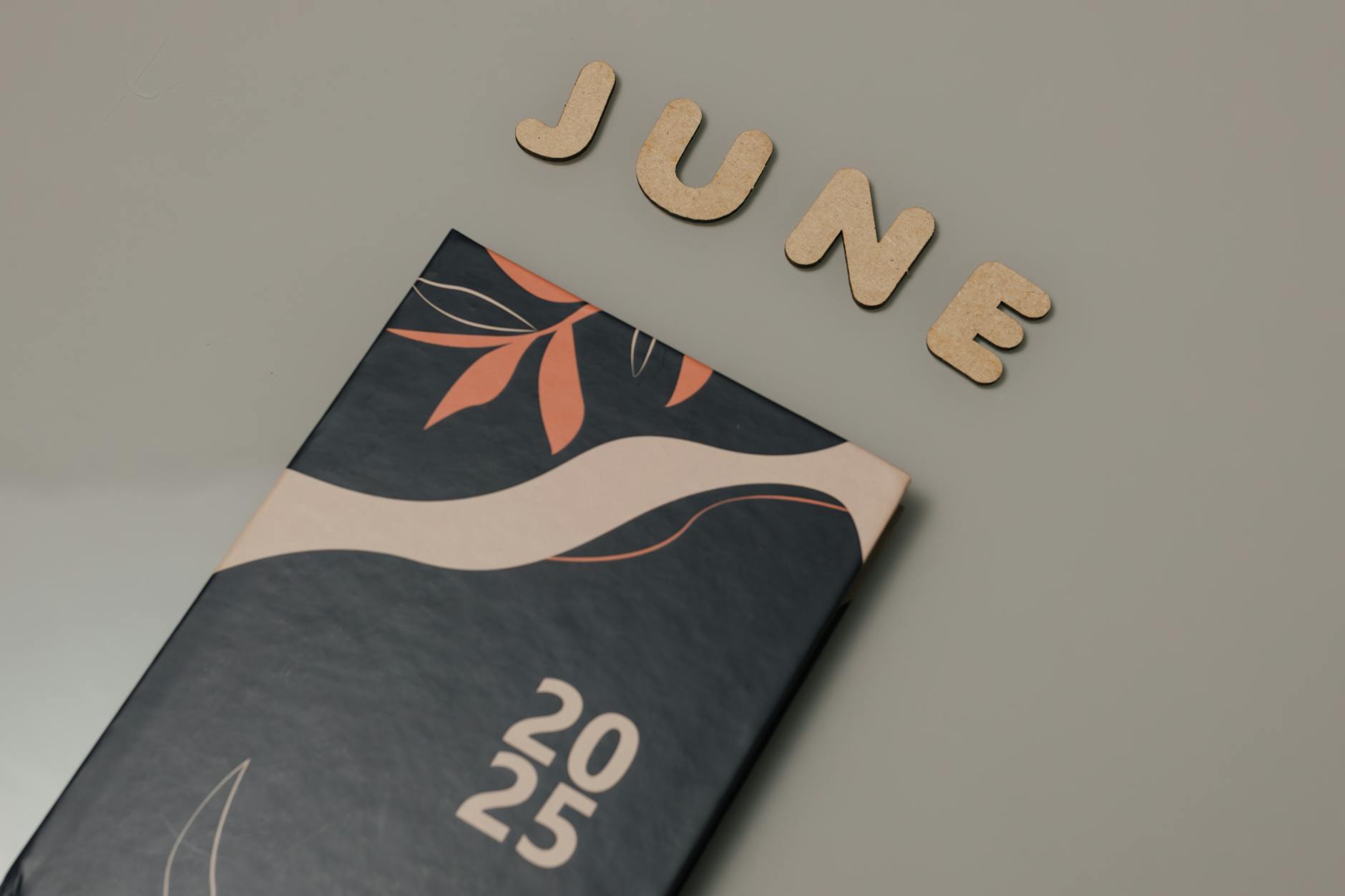 A minimalist 2025 planner with 'June' wooden cut-out letters on a neutral background, ideal for planning and organization.