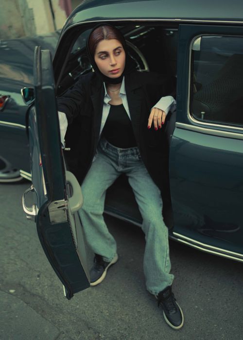 Free Stylish woman stepping out of a vintage car on an urban street, wearing casual attire. Stock Photo