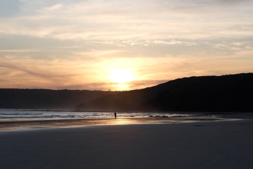 Free A peaceful beach scene at sunset with a lone figure walking along the shoreline. Stock Photo