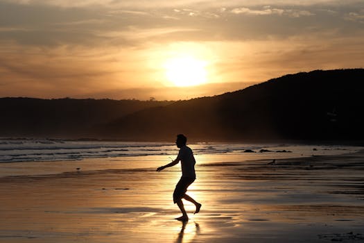 A serene beach scene with a silhouette walking along the shore during sunset.