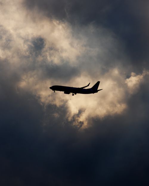 Free Silhouette of an airplane flying amidst dramatic clouds, creating a striking visual contrast. Stock Photo