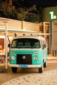 A teal retro Volkswagen van parked outside at night in Nanjing cityscape.