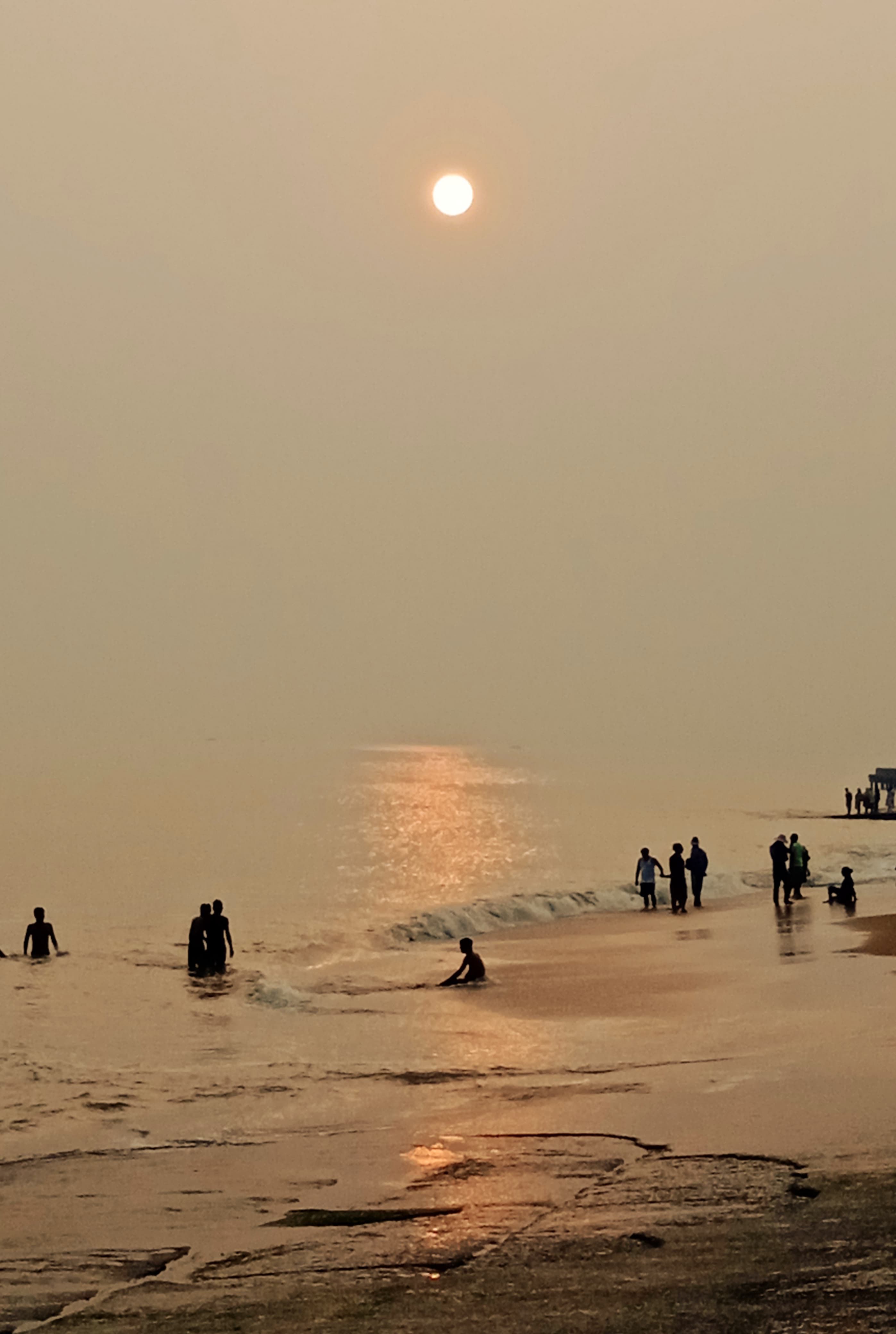 A tranquil sunset over a beach with silhouettes of people enjoying the waves, creating a peaceful atmosphere.