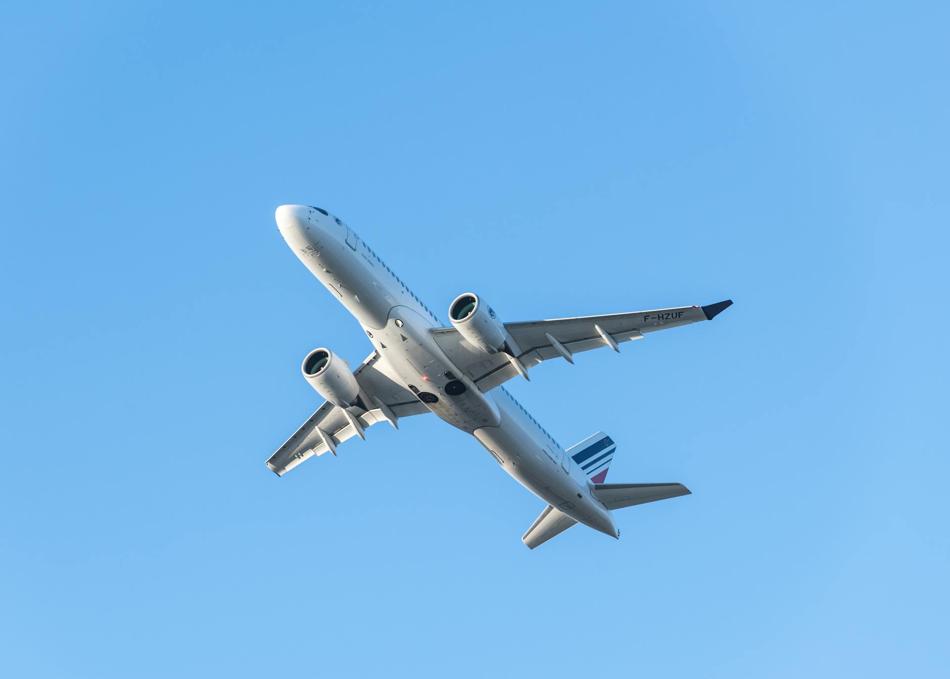 A passenger airplane in flight, captured from below with a clear blue sky background.