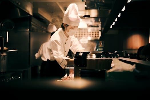 A chef wearing a uniform works diligently in a bustling Japanese restaurant kitchen in Osaka, Japan.