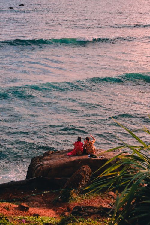 Free A serene moment of a couple sitting on a cliff during sunset overlooking the ocean in Sri Lanka. Stock Photo