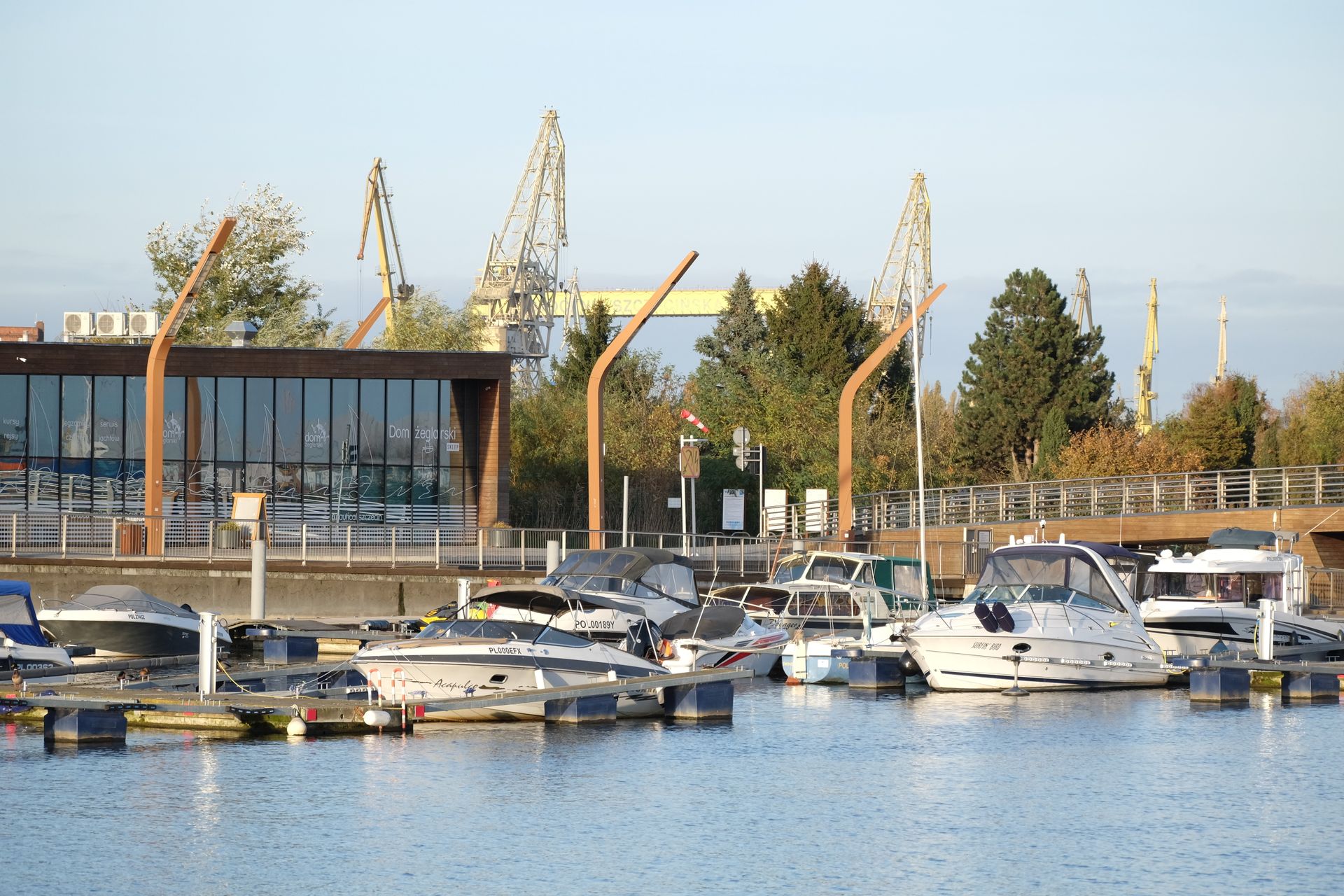 A scenic marina with boats and industrial cranes in the background during sunset.