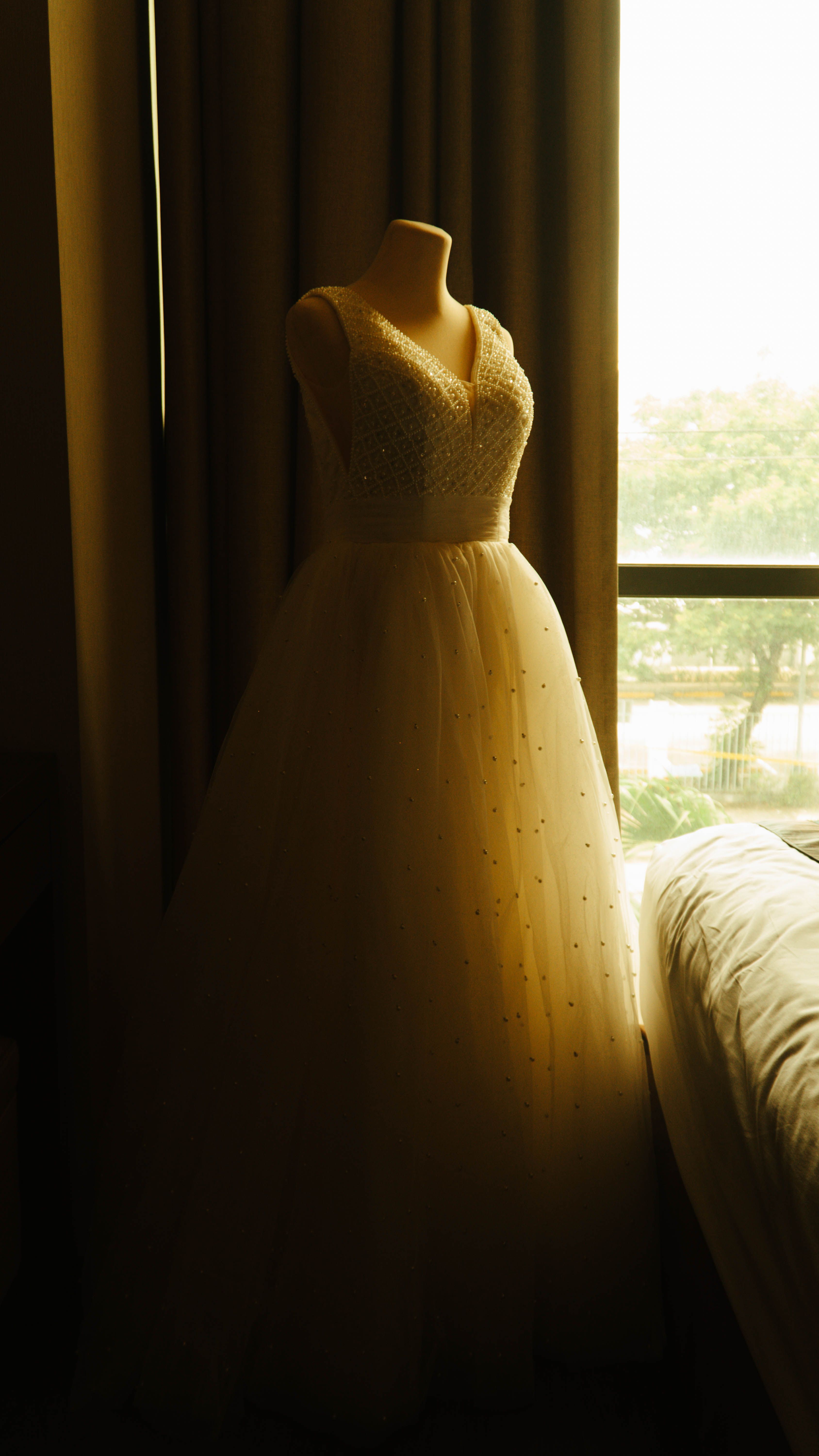 A white bridal gown displayed on a mannequin in a softly lit room by the window.