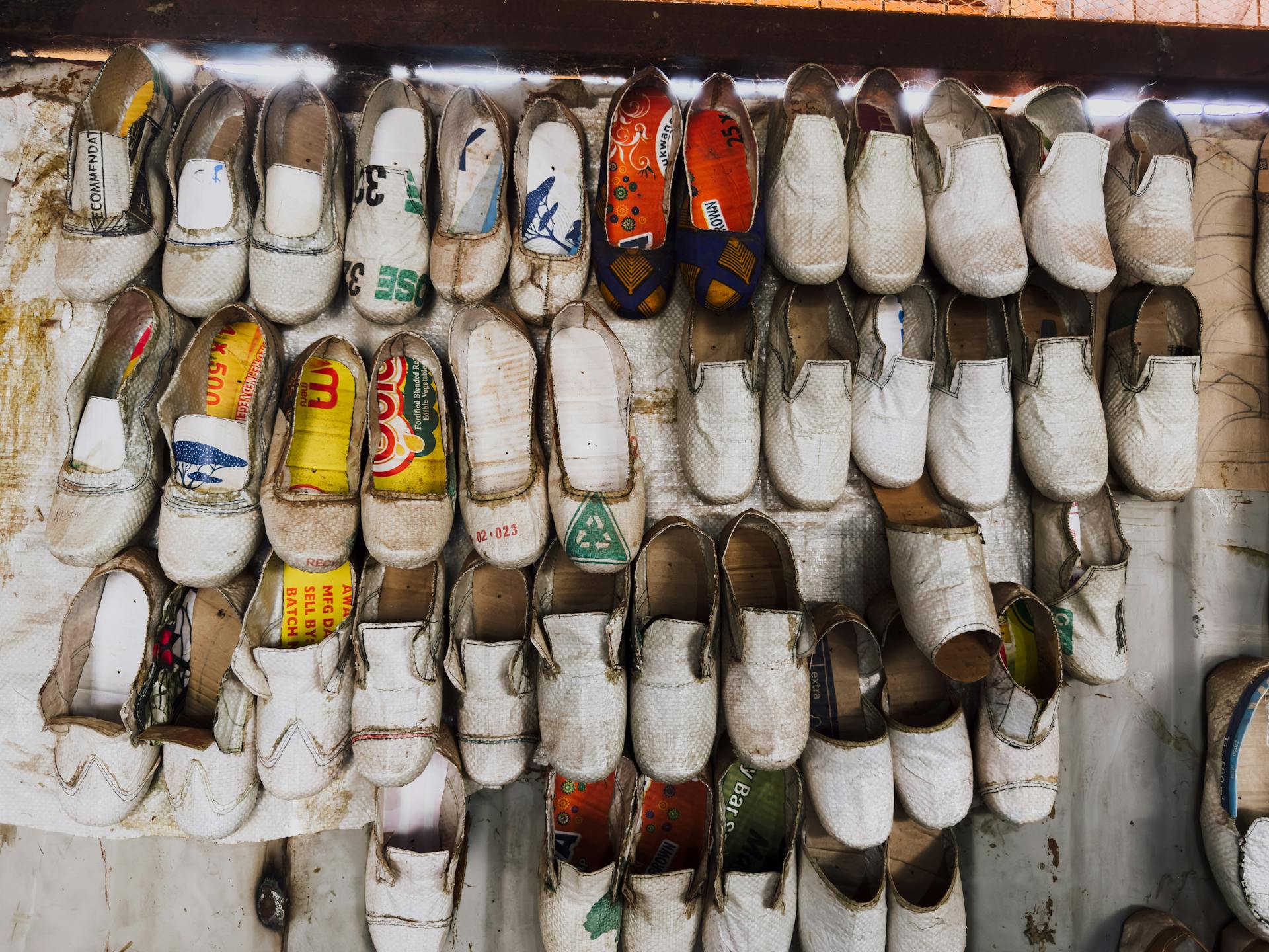 Handcrafted Ugandan shoes with vibrant inner patterns displayed on a rustic rack.