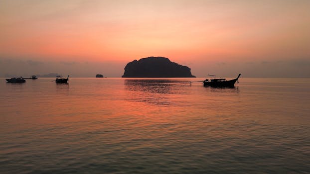 Peaceful sunrise over Phang Nga Bay in Thailand with silhouetted boats and islands.