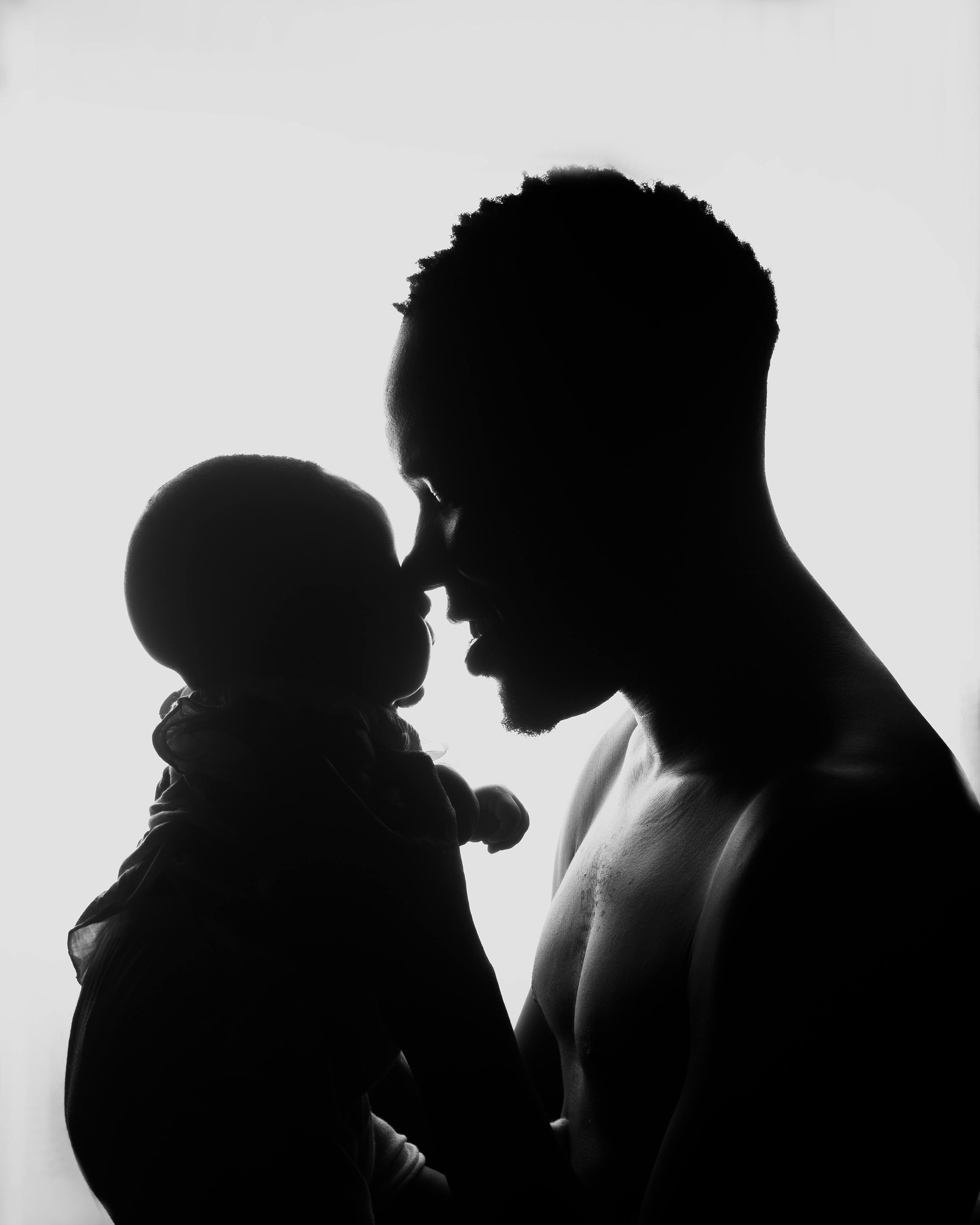 Heartfelt silhouette of a father tenderly embracing his baby against a bright backdrop.