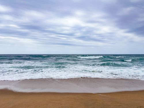 Free Peaceful ocean waves gently wash onto a deserted sandy beach under a cloudy sky. Stock Photo