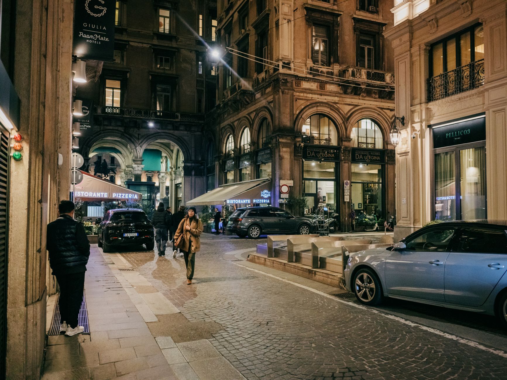 A bustling European city street at night with people, cafes, and shops.