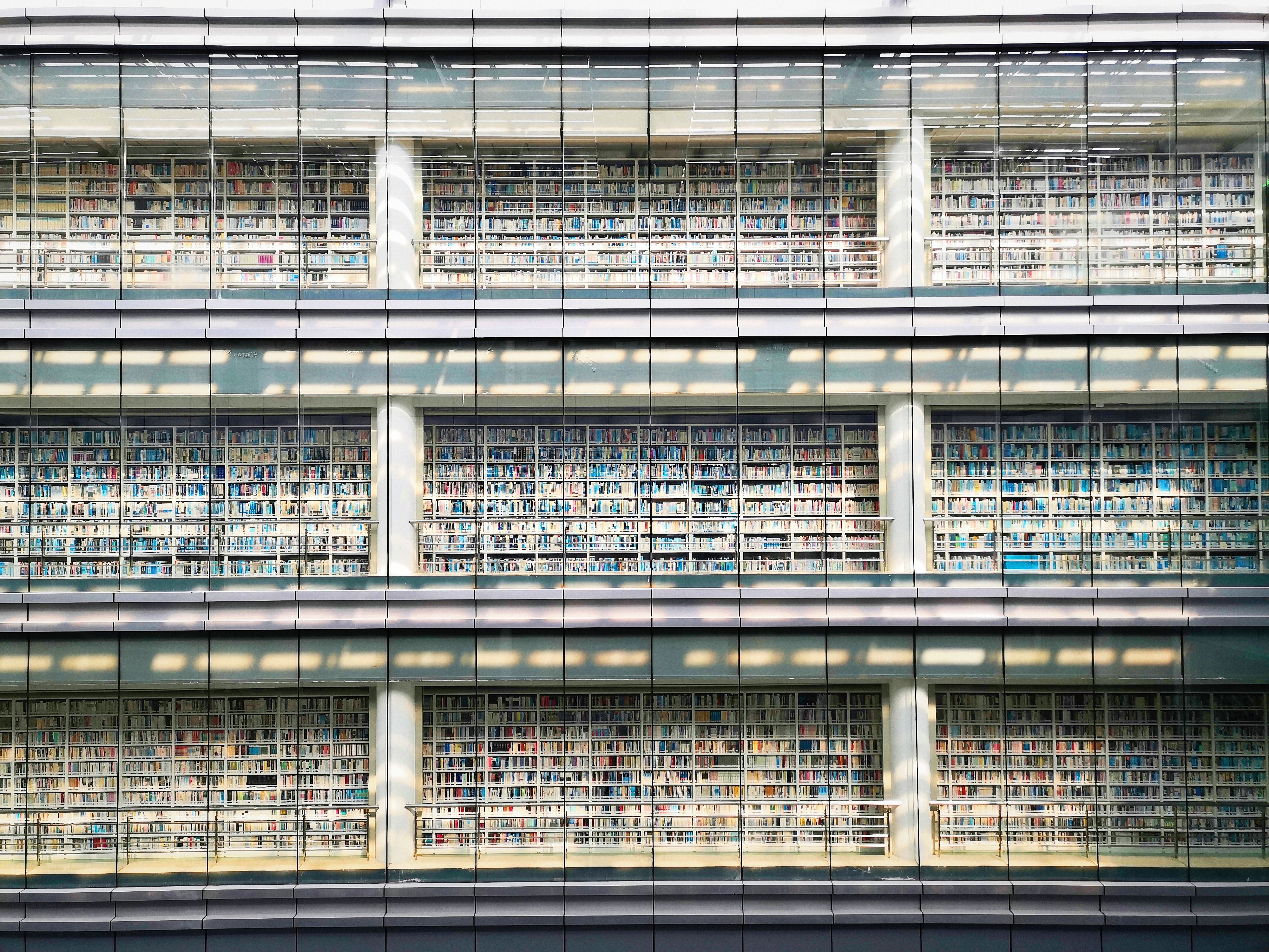 Sunlit view of a modern library facade with multiple levels of bookshelves behind glass walls.