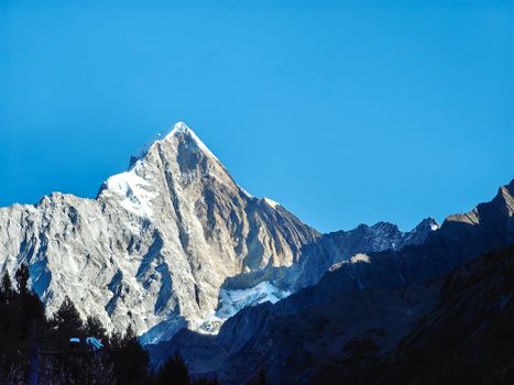 A stunning view of a snow-capped mountain peak against a clear blue sky, captured at sunrise.