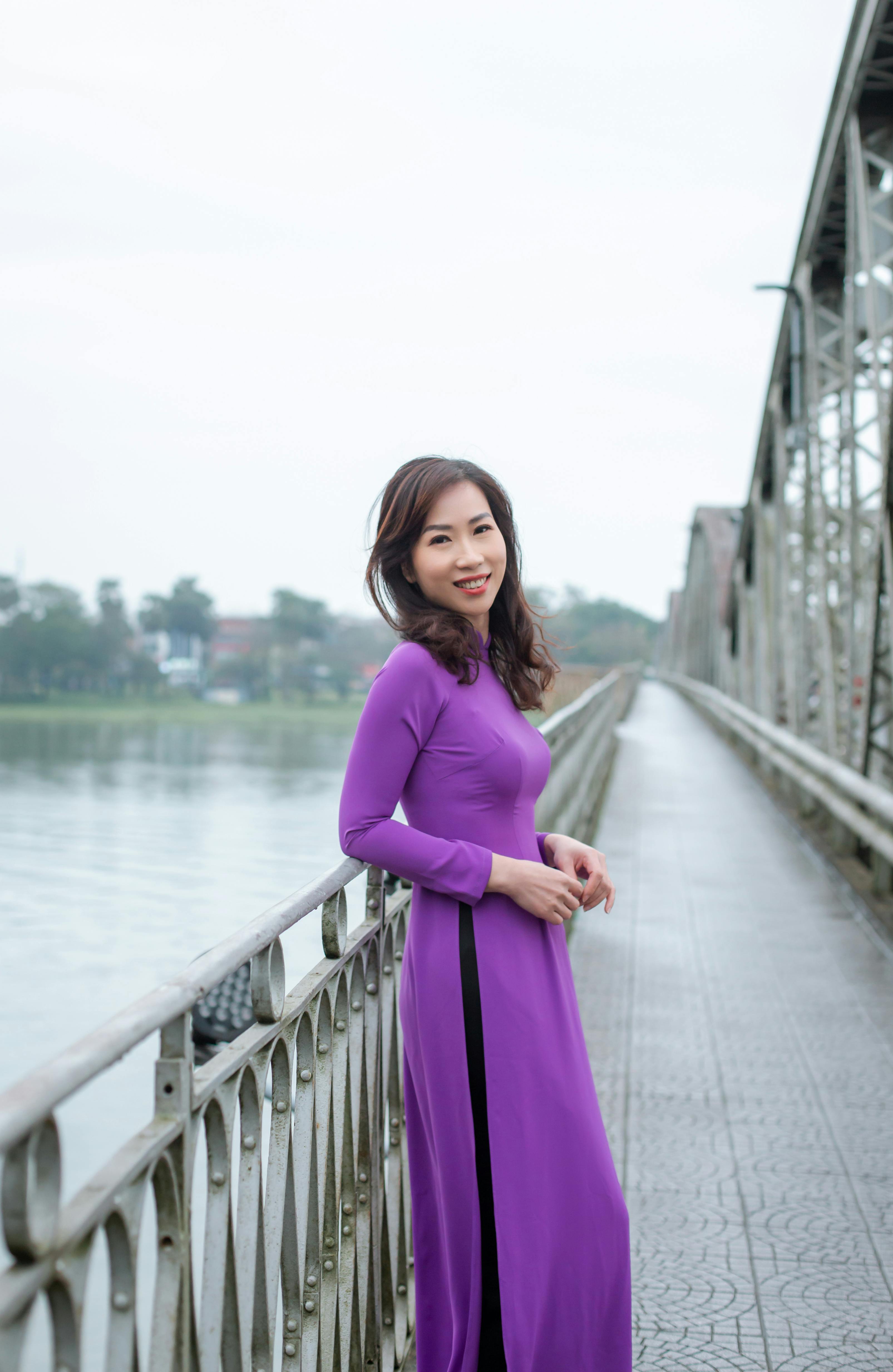 A woman in a purple traditional dress poses on a bridge in Huế, Vietnam.