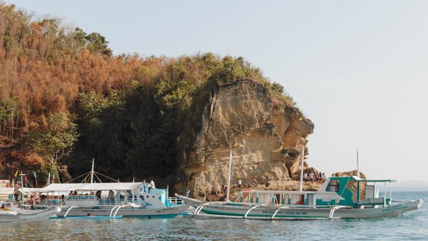 Boats docked along a picturesque cliff in Santa Cruz, Philippines, under a clear sky.
