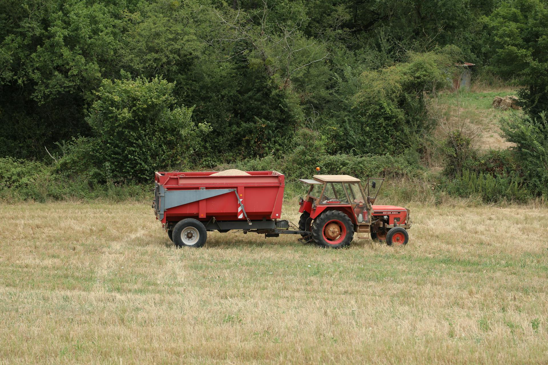 A vibrant red tractor towing a trailer on a lush green field, ideal for agriculture themes.
