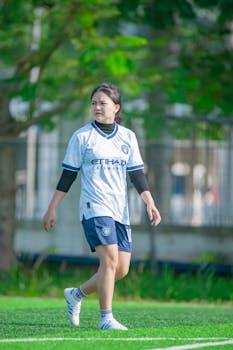 A young woman in a soccer outfit walking on a green field in Hanoi.