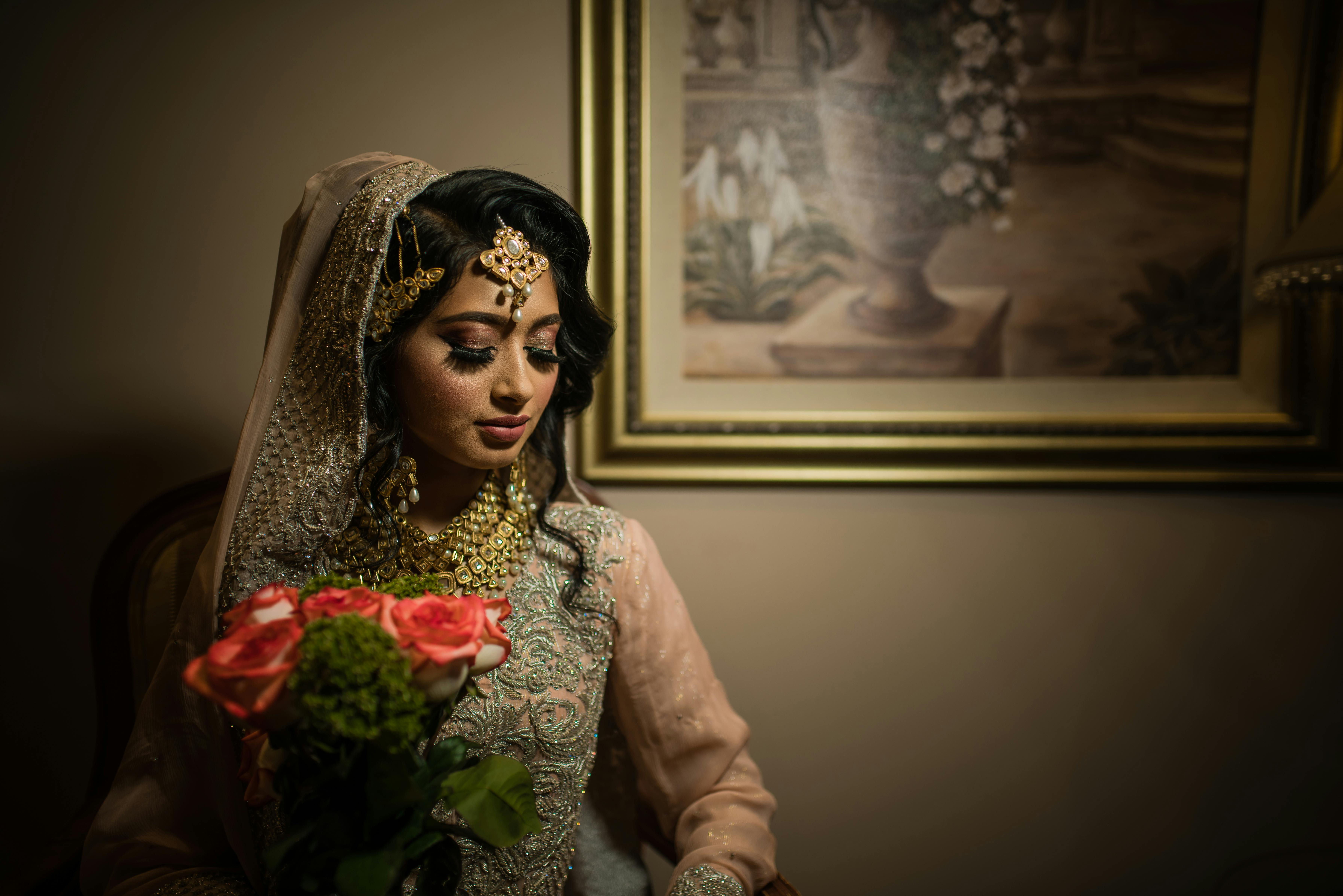 South Asian bride in traditional attire holding flowers in an elegant setting.