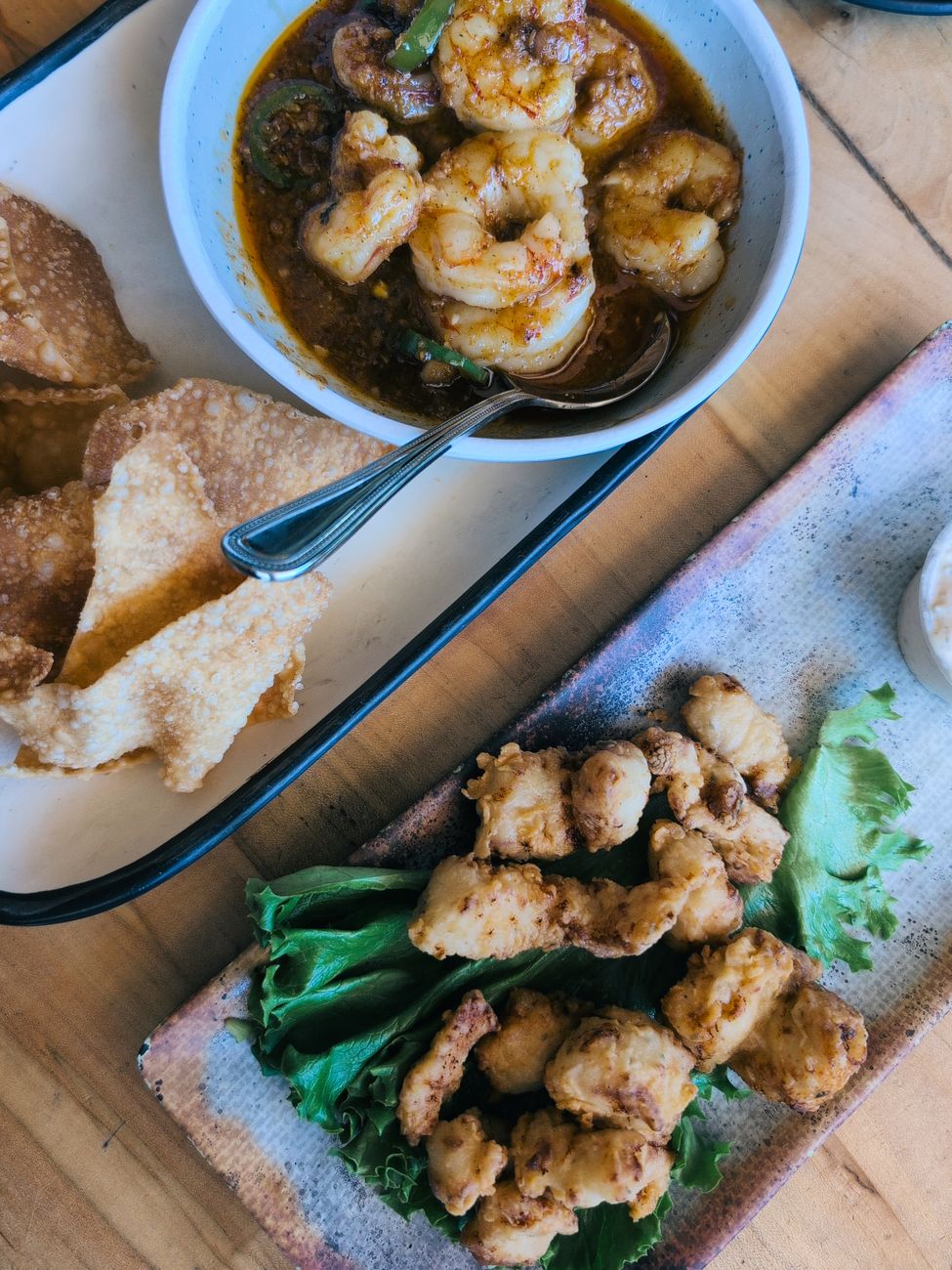 A bowl of creamy white grits topped with pink gulf shrimp in a rich brown sauce with diced ham and vegetables, garnished with sliced green onions