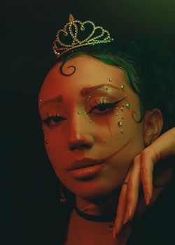 Close-up portrait of a woman with creative makeup and crown in low light.