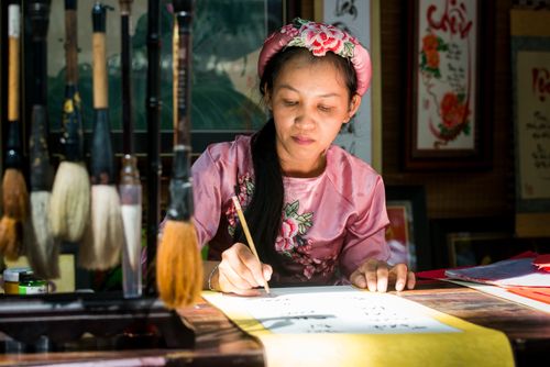 Free A focused woman practicing traditional Vietnamese calligraphy indoors with brushes. Stock Photo