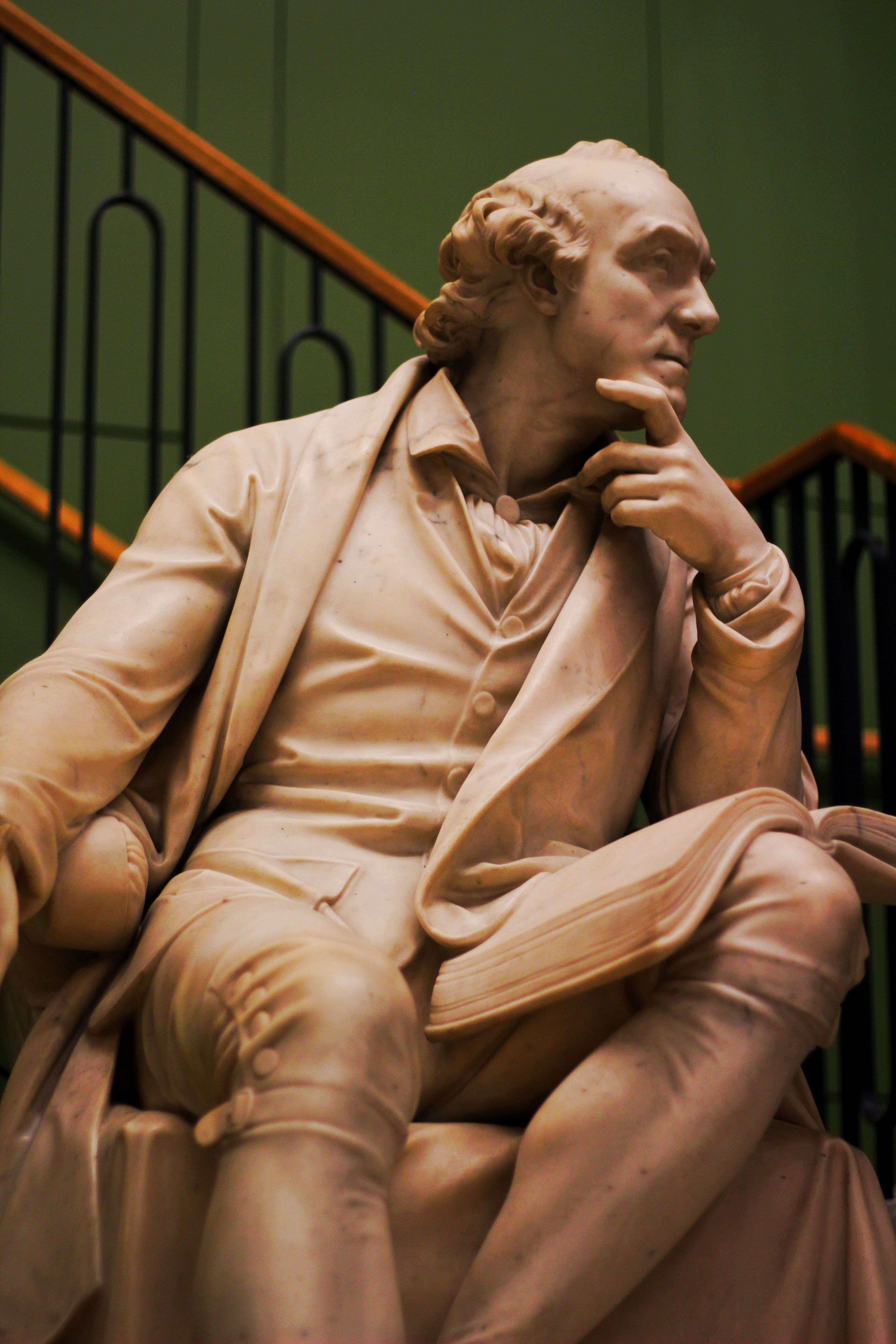 A marble statue depicting a thoughtful figure seated indoors, exuding elegance.
