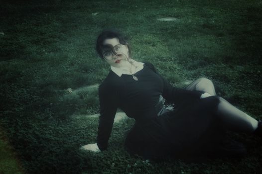 Moody portrait of a woman lying on grass in an artistic, vintage style.