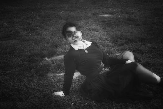 A black and white portrait of a female model with a gothic aesthetic, posing outdoors in a dramatic, moody setting.