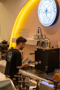 Barista making coffee in a trendy cafe with modern decor and warm lighting.