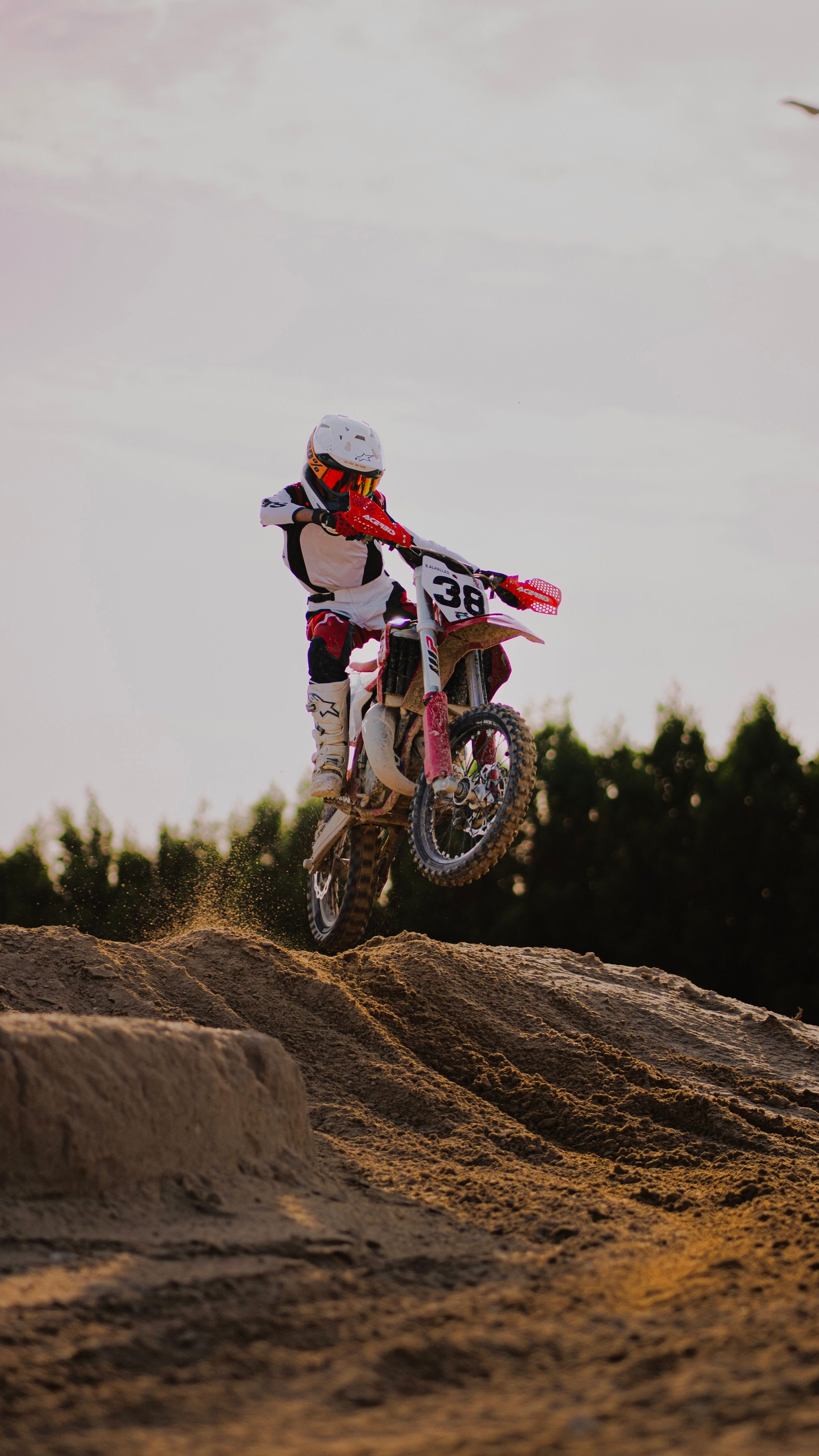 Dynamic motocross rider jumping on dirt track with full gear.