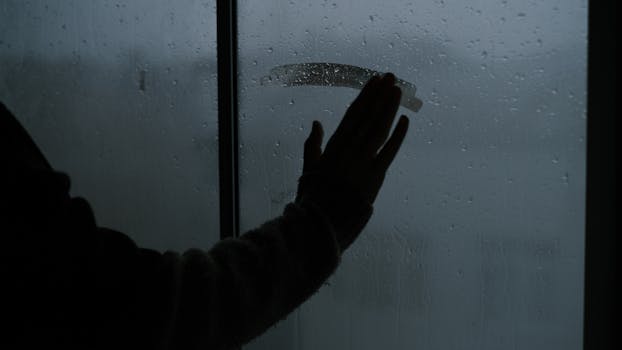 A hand touching a rainy, steamy window creating a melancholic indoor atmosphere.
