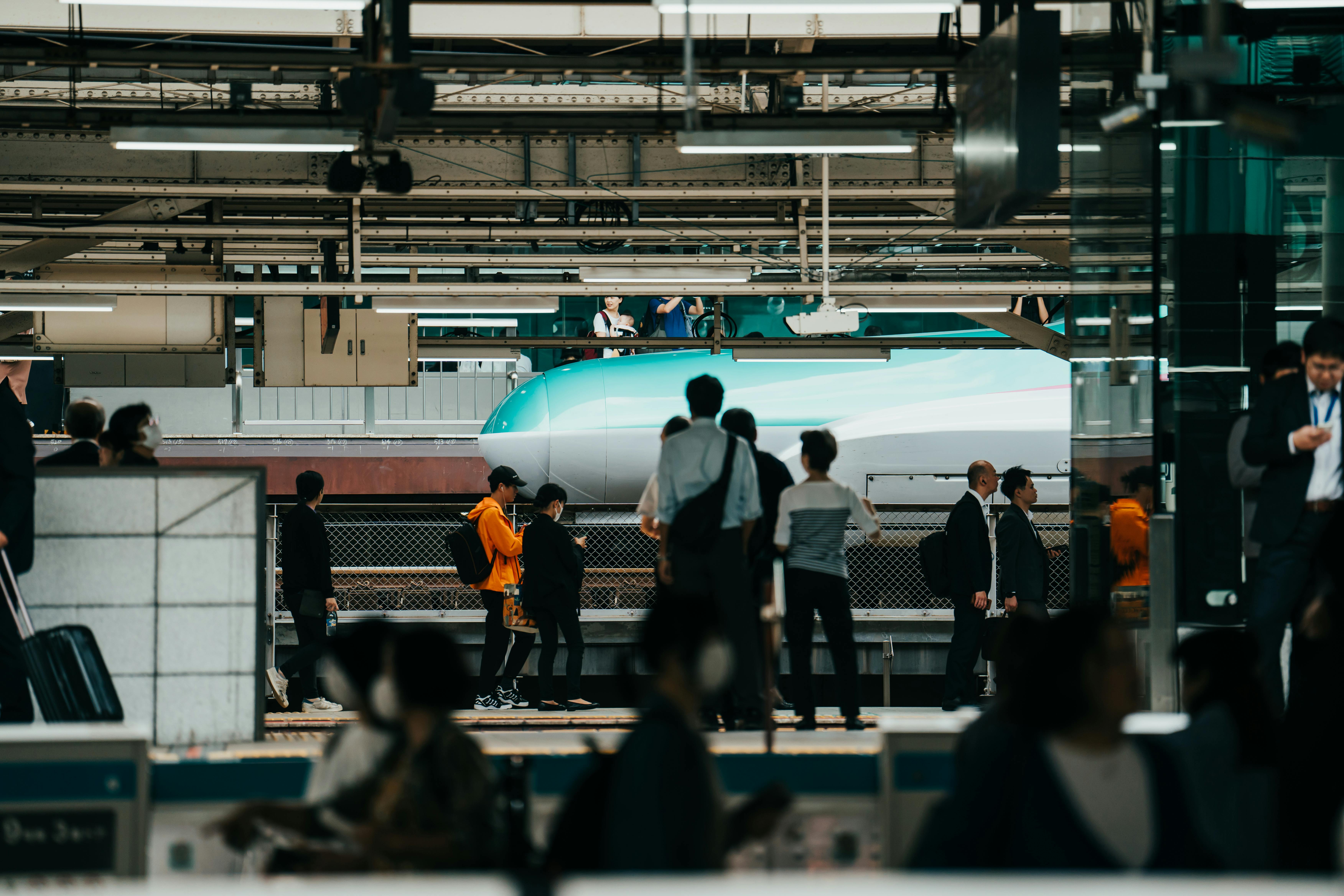 Crowd of people waiting at a bustling Japanese train station with a shinkansen passing by.
