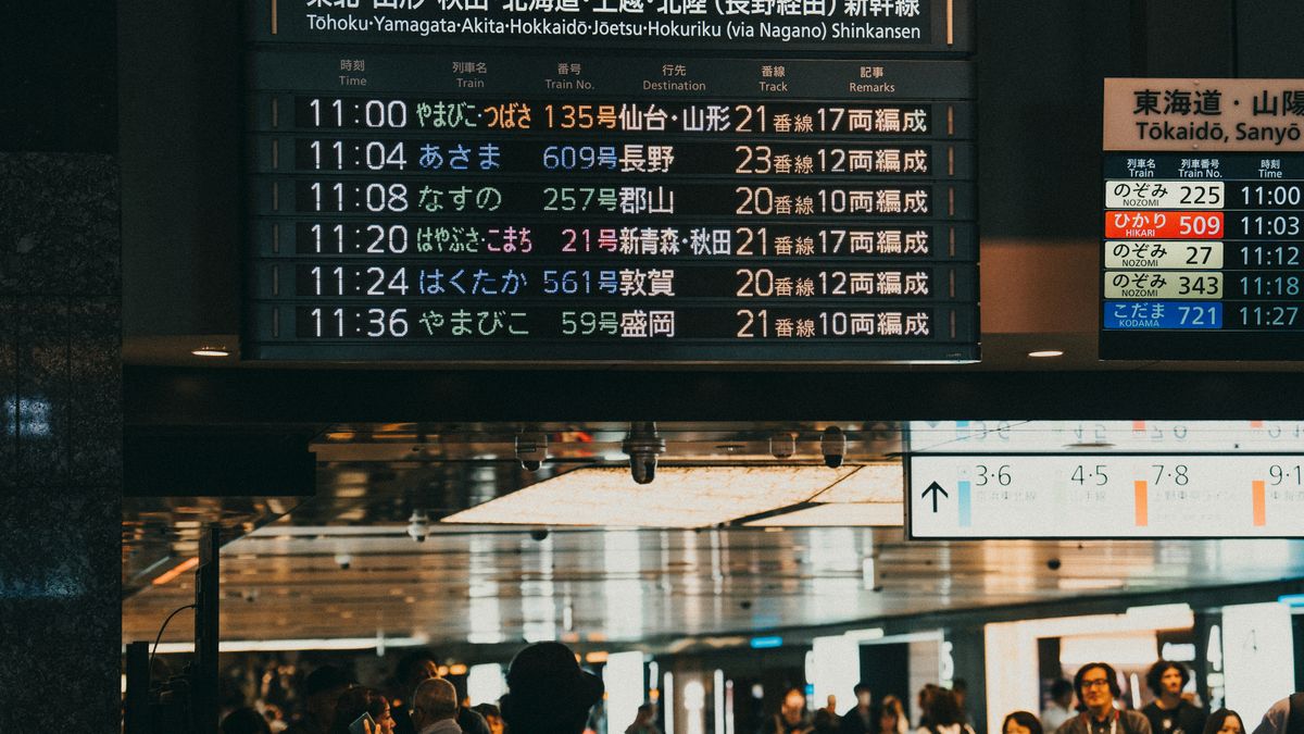 Busy train station in Japan with a digital departure board showing schedules.