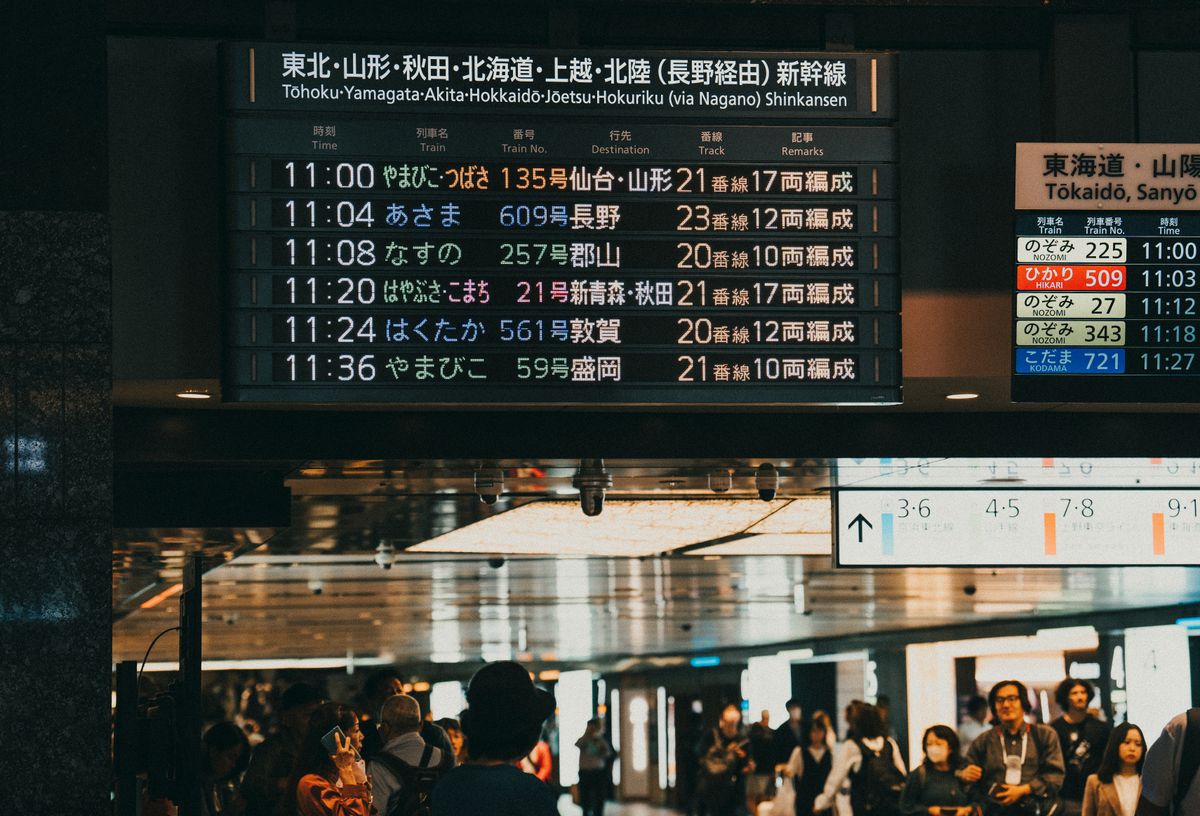 A busy Asian train station with a digital departure board displaying schedules