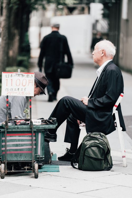 Free Man receiving a shoe shine on a bustling street in Japan, depicting daily life. Stock Photo