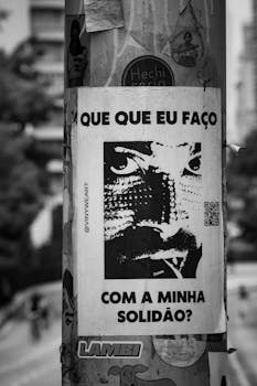 A black and white poster with text and portrait on a pole, street view.