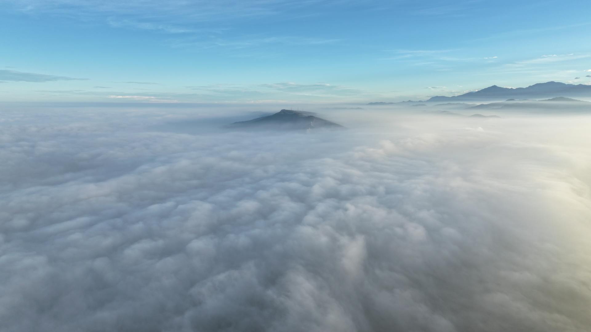 Breathtaking aerial view of mountain peaks emerging through a sea of clouds under a clear blue sky.