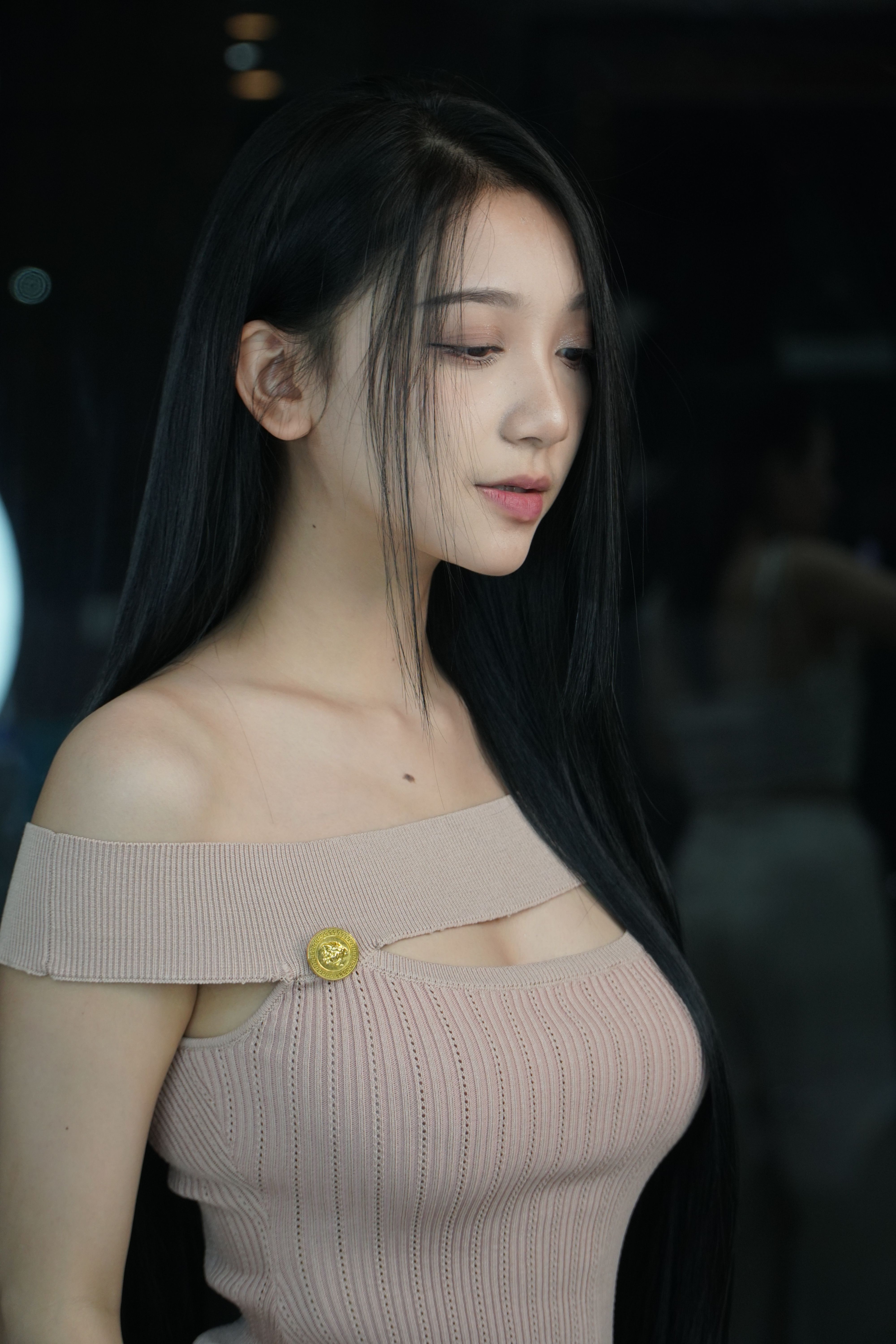 Portrait of a young woman with long black hair in a beige off-shoulder dress, posing gracefully indoors.