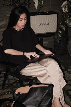 A young woman sits outdoors at night, focused on her laptop under ambient lighting.