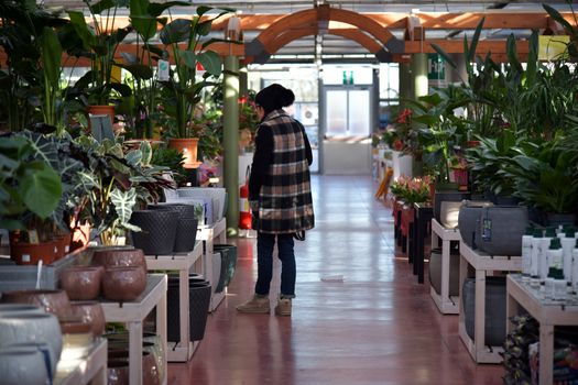 Woman browsing plants in a well-lit garden center filled with vibrant greenery.