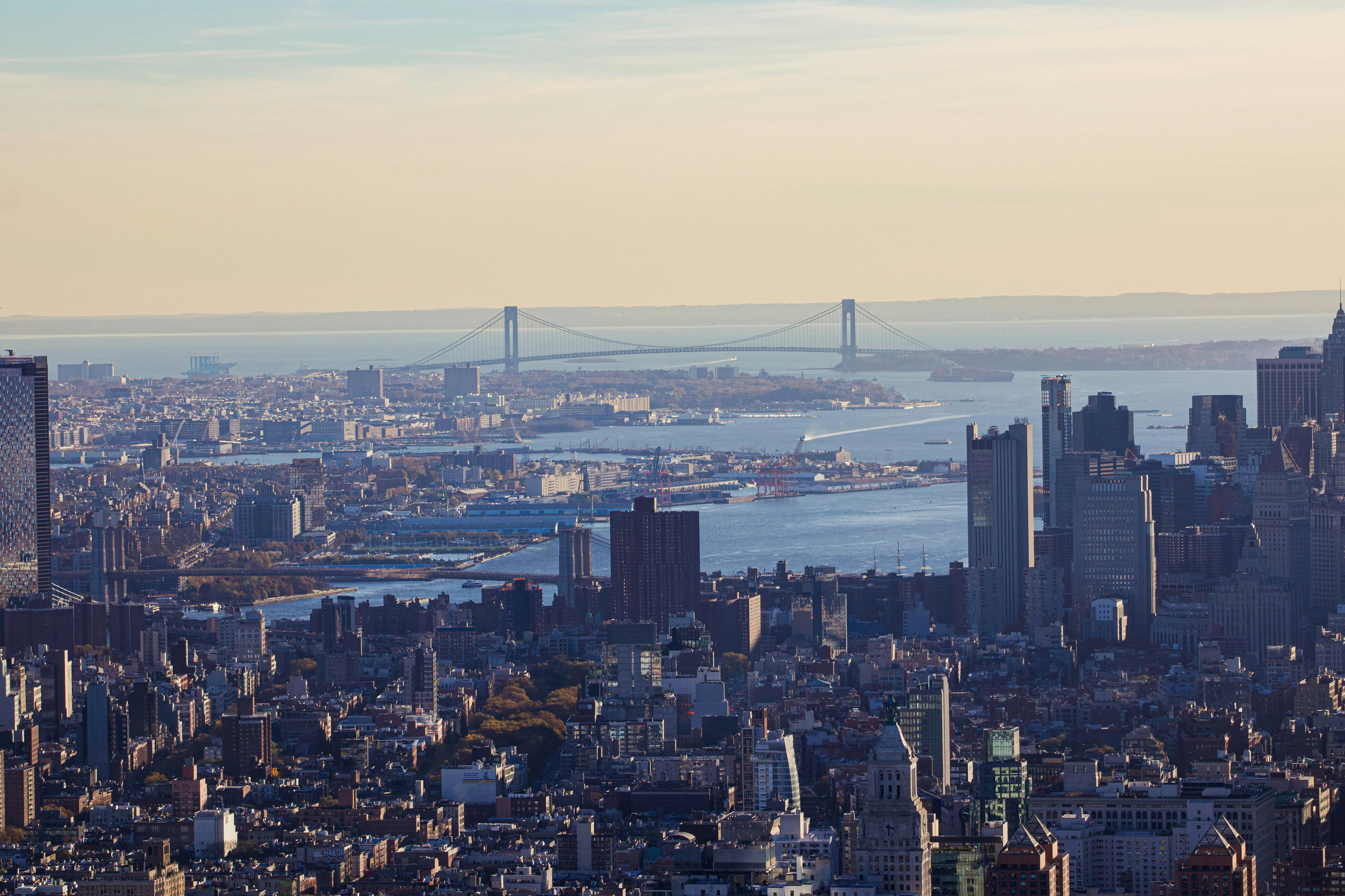 A breathtaking aerial view of New York City skyline with the iconic Verrazzano-Narrows Bridge in the background.