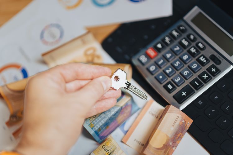 Mano sosteniendo una llave sobre billetes de euro y una calculadora, simbolizando la inversión inmobiliaria.