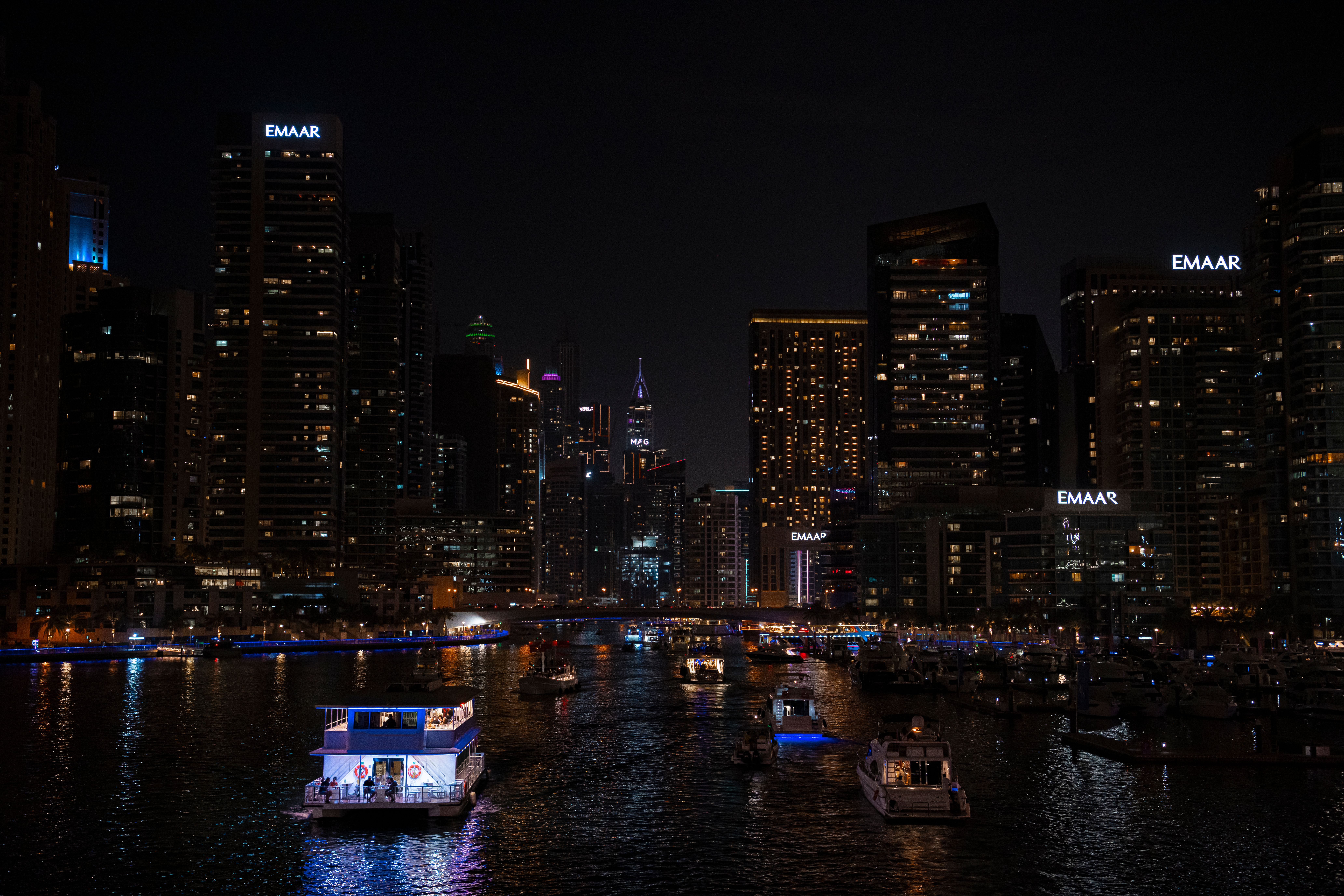 Illuminated Dubai Marina skyline at night with boats on the water.